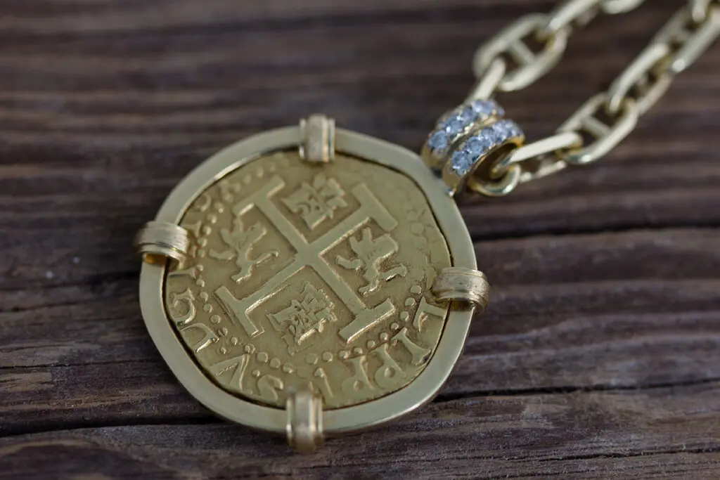 Золотая испанская монета в форме кулона весом 18 карат, висящая на цепочке.